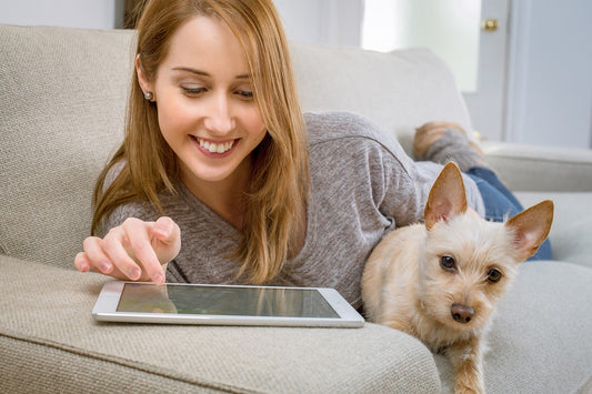 A woman browsing BinxBerry Consignment's online thrift shop while relaxing with her dog on her couch